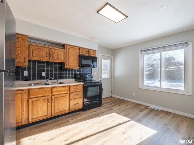 kitchen featuring black appliances, backsplash, sink, and light hardwood / wood-style flooring