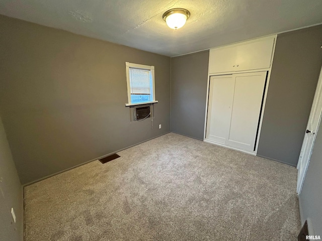 unfurnished bedroom with a textured ceiling, light colored carpet, a closet, and cooling unit