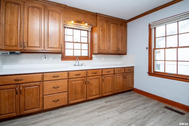 kitchen featuring a healthy amount of sunlight, sink, light wood-type flooring, and ornamental molding