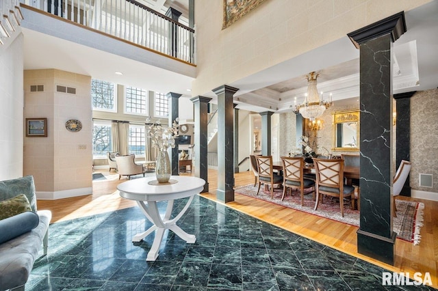 living room with a towering ceiling, ornate columns, ornamental molding, hardwood / wood-style flooring, and an inviting chandelier