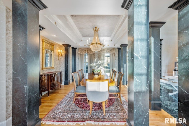 dining space with a notable chandelier, decorative columns, crown molding, a tray ceiling, and hardwood / wood-style flooring