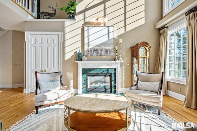 sitting room with a wealth of natural light, a towering ceiling, a premium fireplace, and hardwood / wood-style flooring