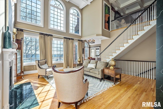 living room with beam ceiling, coffered ceiling, a high end fireplace, a towering ceiling, and wood-type flooring