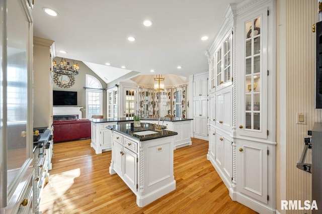 kitchen with dark stone counters, a center island, light hardwood / wood-style floors, white cabinetry, and lofted ceiling