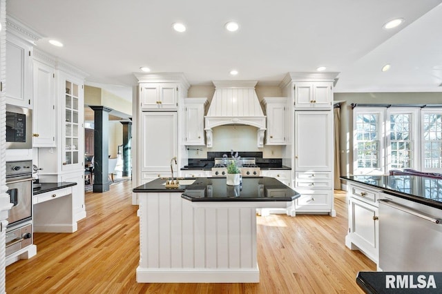 kitchen with a center island, premium range hood, white cabinets, light wood-type flooring, and stainless steel appliances