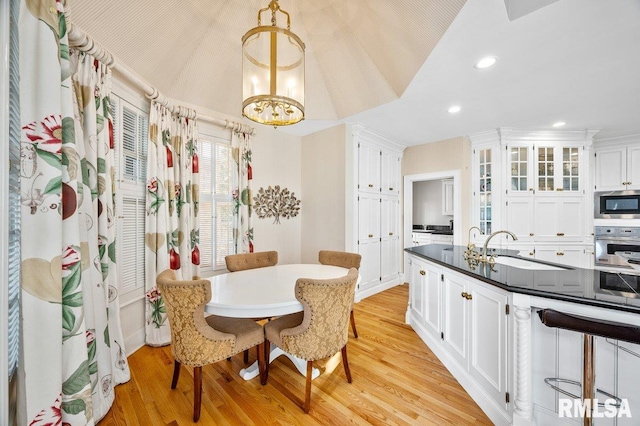 dining room featuring a notable chandelier, light hardwood / wood-style floors, lofted ceiling, and sink