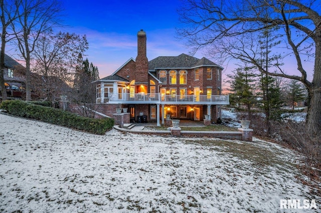 snow covered rear of property featuring a patio and a balcony