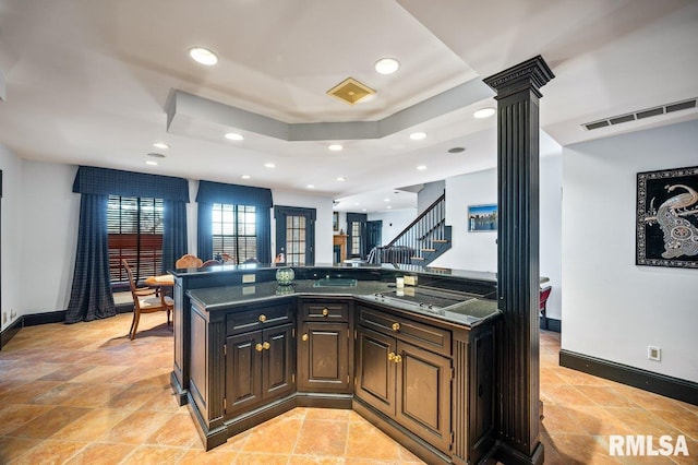 kitchen with dark stone counters, stainless steel cooktop, a tray ceiling, and ornate columns