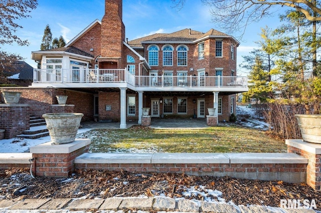 snow covered back of property with a lawn, a patio, and a wooden deck