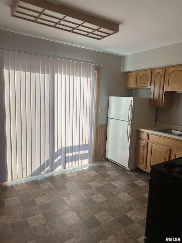 kitchen featuring white fridge, black stove, sink, and light brown cabinetry