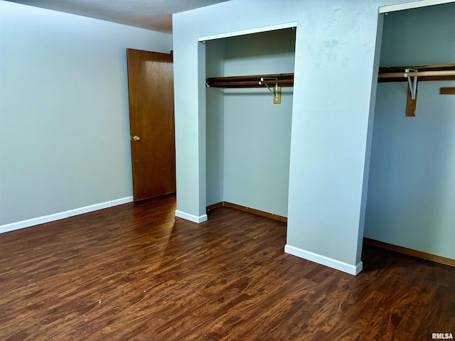 unfurnished bedroom featuring two closets, baseboards, and wood finished floors