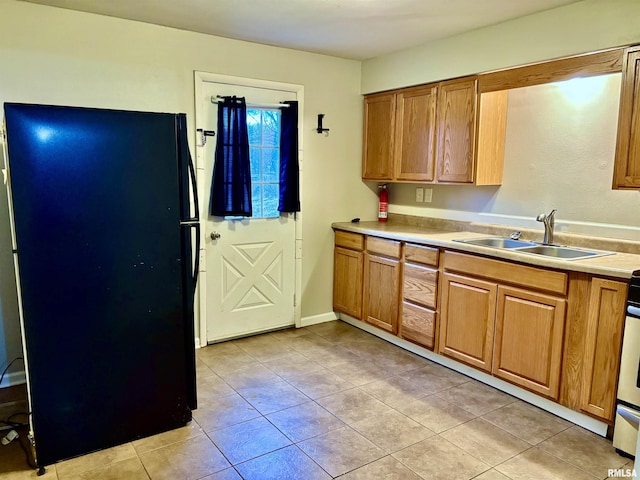 kitchen with light countertops, a sink, freestanding refrigerator, and brown cabinets