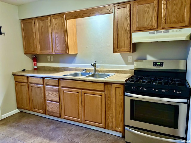 kitchen featuring stainless steel gas range, brown cabinetry, a sink, and under cabinet range hood