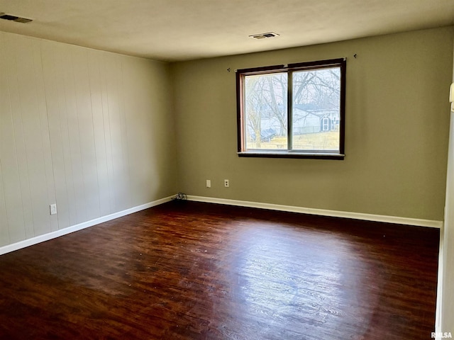 spare room with dark wood-type flooring, visible vents, and baseboards