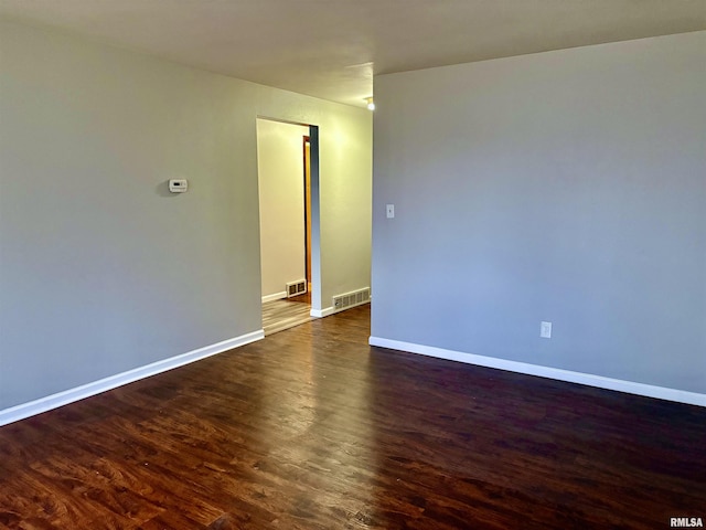 unfurnished room with dark wood-style flooring, visible vents, and baseboards