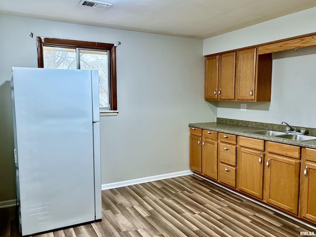 kitchen with brown cabinets, visible vents, freestanding refrigerator, a sink, and wood finished floors