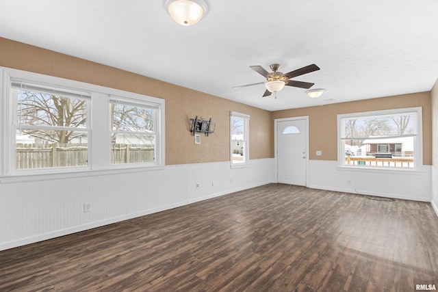 unfurnished living room with plenty of natural light, dark wood-type flooring, and ceiling fan