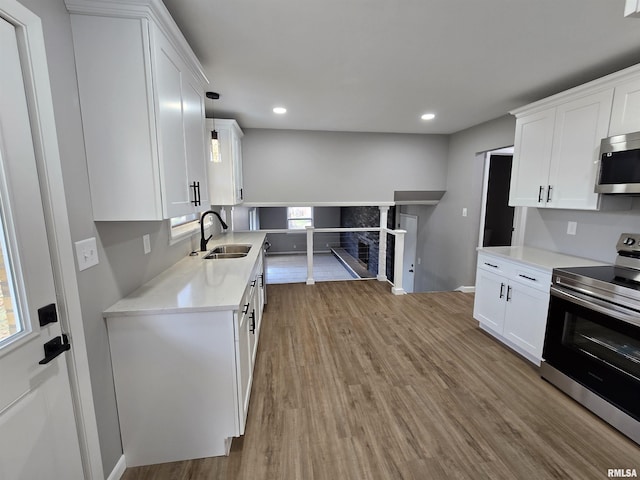 kitchen featuring sink, appliances with stainless steel finishes, decorative light fixtures, light hardwood / wood-style floors, and white cabinetry