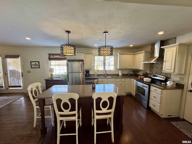 kitchen with a center island, wall chimney range hood, hanging light fixtures, and appliances with stainless steel finishes