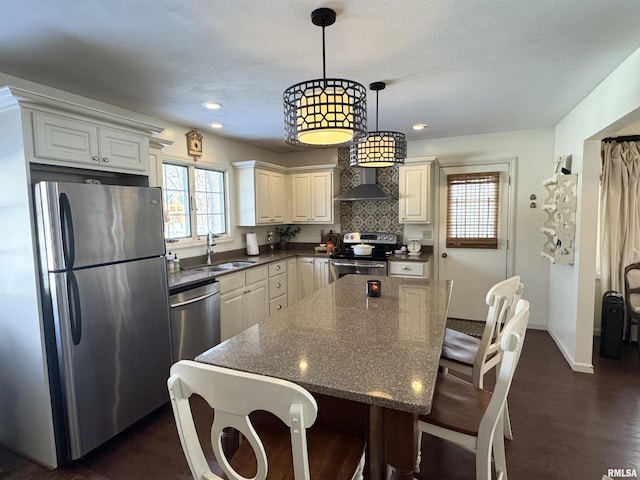 kitchen with sink, hanging light fixtures, wall chimney exhaust hood, dark stone countertops, and stainless steel appliances