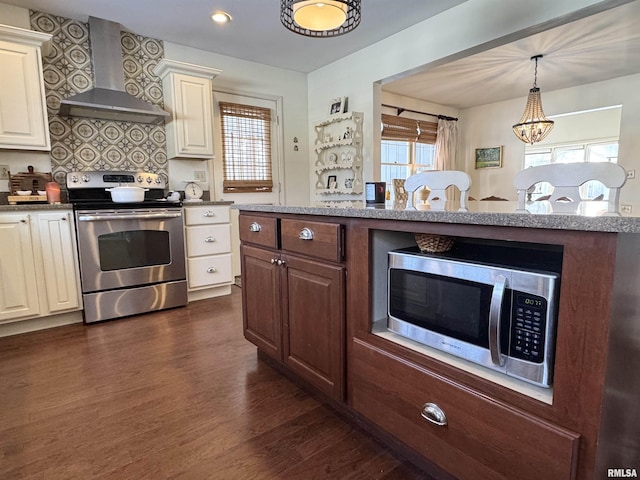 kitchen featuring pendant lighting, dark wood-type flooring, wall chimney range hood, a notable chandelier, and stainless steel appliances