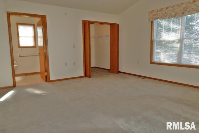 unfurnished bedroom with ensuite bath, a closet, light colored carpet, and multiple windows