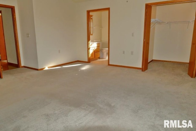 unfurnished bedroom with ensuite bathroom, a walk in closet, light carpet, and a closet