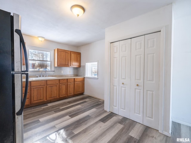 kitchen with decorative backsplash, black fridge, sink, and light hardwood / wood-style flooring