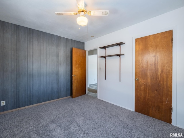 unfurnished bedroom with carpet, ceiling fan, wooden walls, and a closet