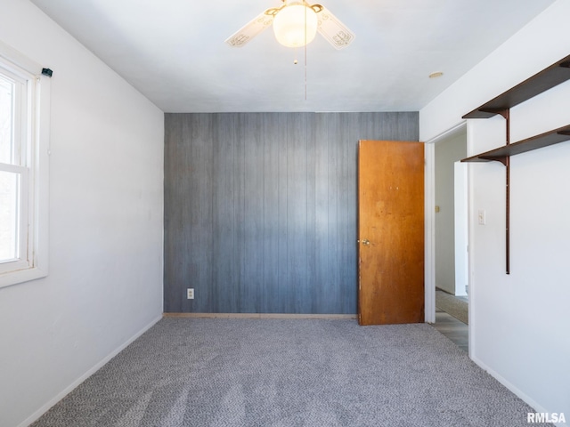 carpeted empty room featuring ceiling fan, wooden walls, and a healthy amount of sunlight