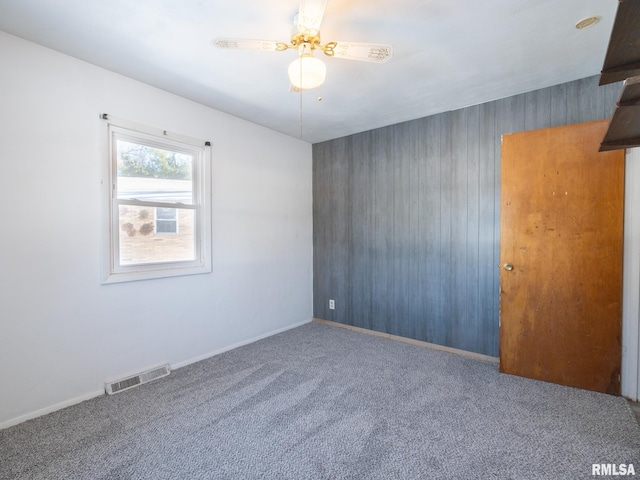 carpeted spare room featuring ceiling fan and wood walls