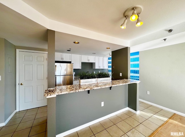 kitchen with white cabinets, light tile patterned floors, light stone countertops, a breakfast bar area, and stainless steel refrigerator