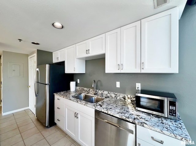 kitchen featuring light stone counters, stainless steel appliances, sink, light tile patterned floors, and white cabinets