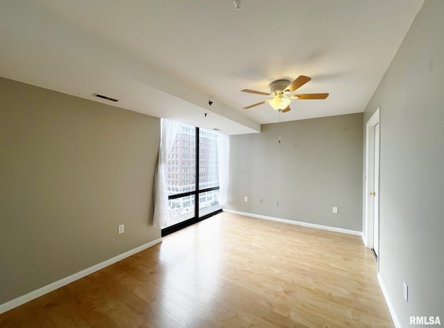 empty room featuring ceiling fan, light hardwood / wood-style flooring, and a wall of windows