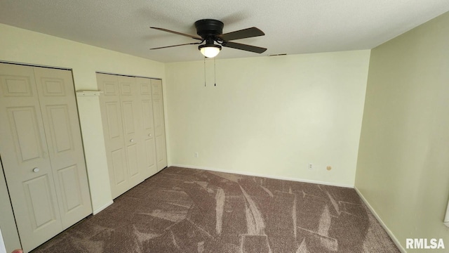 unfurnished bedroom featuring ceiling fan, dark carpet, a textured ceiling, and two closets