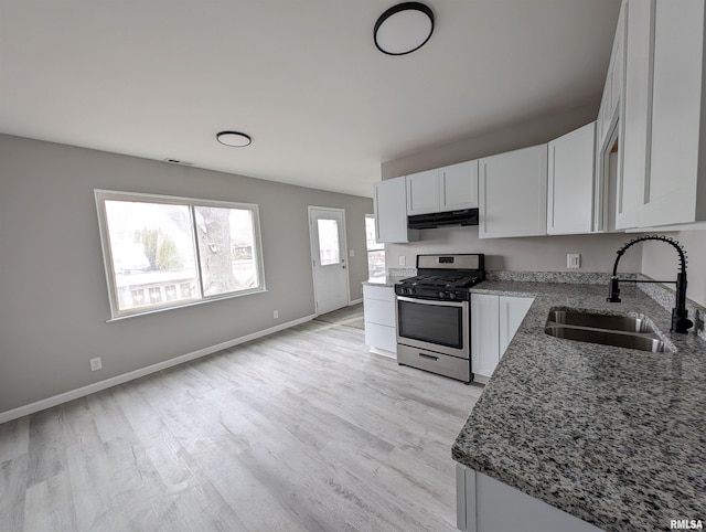 kitchen featuring stainless steel gas stove, sink, white cabinets, light stone counters, and light wood-type flooring