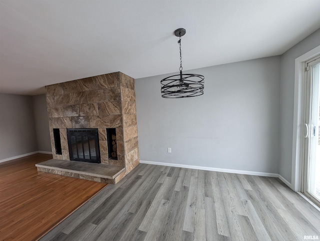 unfurnished living room with a fireplace, light wood-type flooring, a chandelier, and a wealth of natural light