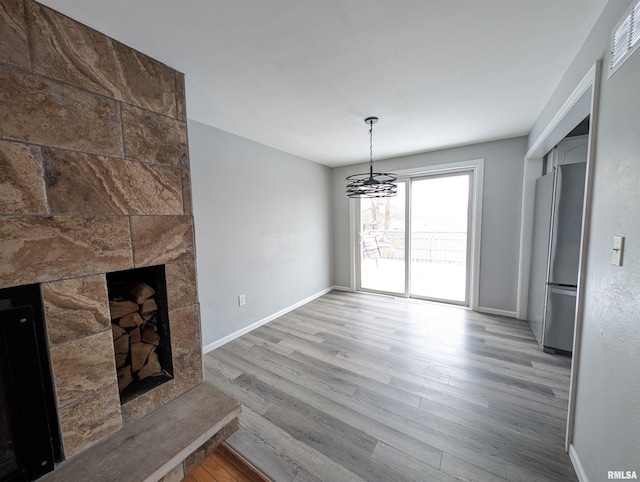 unfurnished living room featuring a chandelier, light wood-type flooring, and a stone fireplace