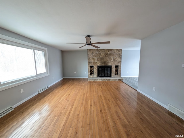 unfurnished living room with ceiling fan, a stone fireplace, light wood-type flooring, and a baseboard radiator