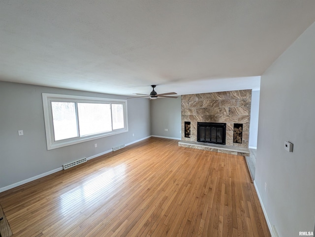 unfurnished living room with a stone fireplace, ceiling fan, and light hardwood / wood-style flooring