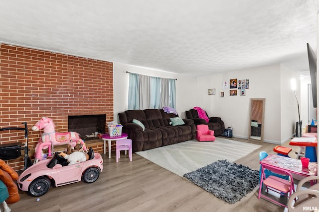 living room with wood-type flooring, a textured ceiling, and a brick fireplace