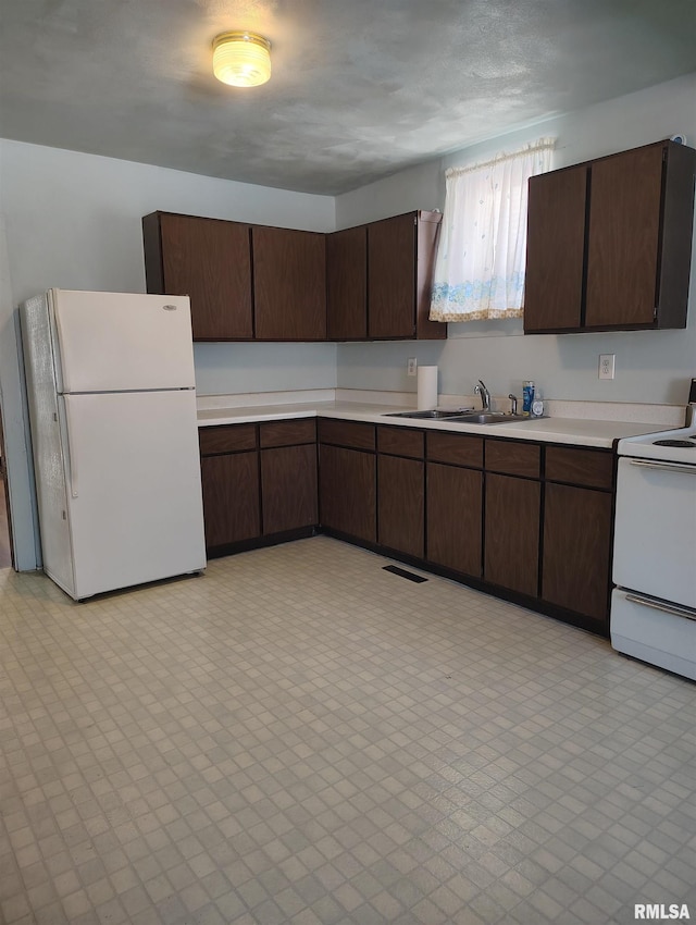 kitchen with white appliances, dark brown cabinetry, and sink