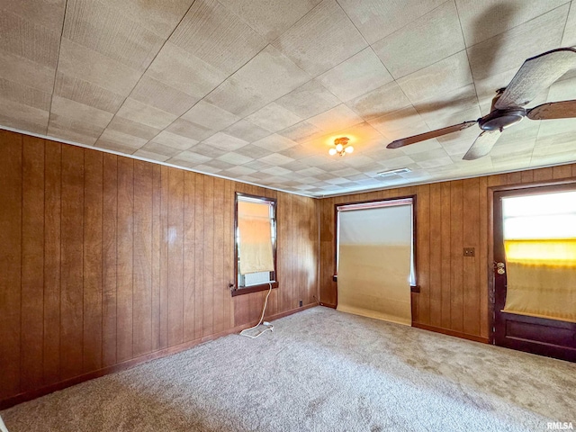 unfurnished room featuring wood walls, ceiling fan, and light carpet