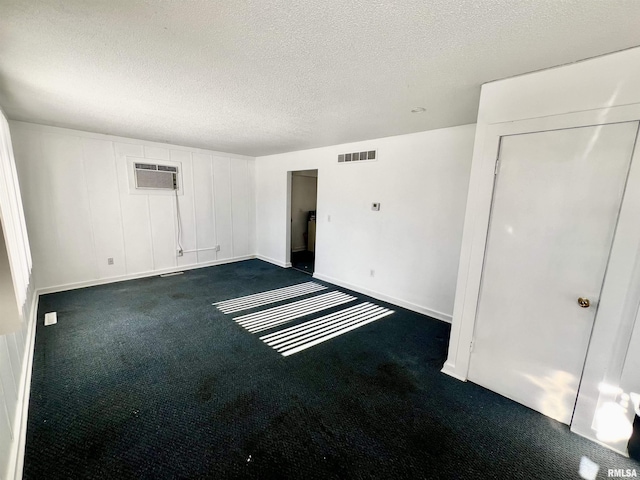 unfurnished room with a wall unit AC, a textured ceiling, and dark colored carpet