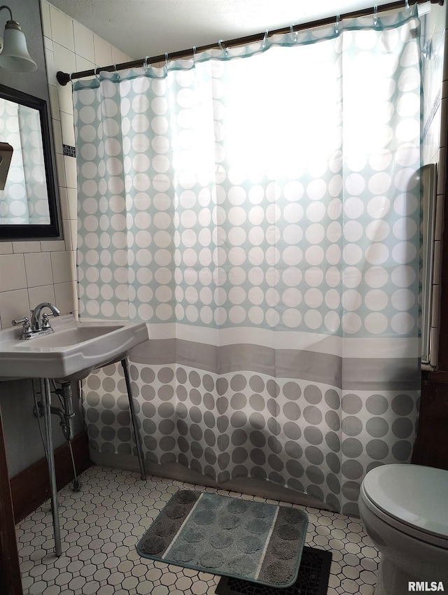 full bath with a sink, tile patterned flooring, curtained shower, tile walls, and toilet