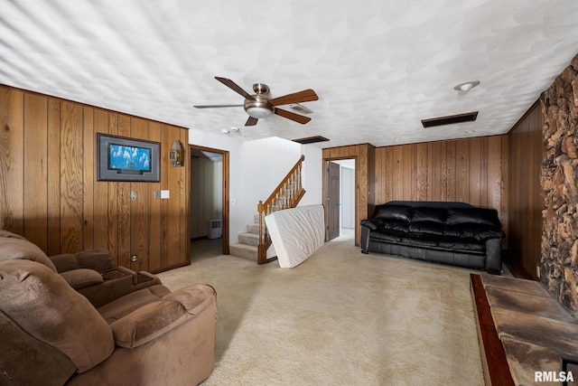 living room with wooden walls, a textured ceiling, ceiling fan, and light colored carpet