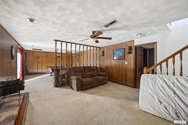 carpeted living room with a textured ceiling, wood walls, and ceiling fan