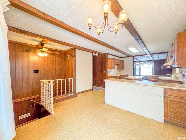 kitchen with a textured ceiling, decorative light fixtures, wooden walls, ceiling fan with notable chandelier, and beamed ceiling