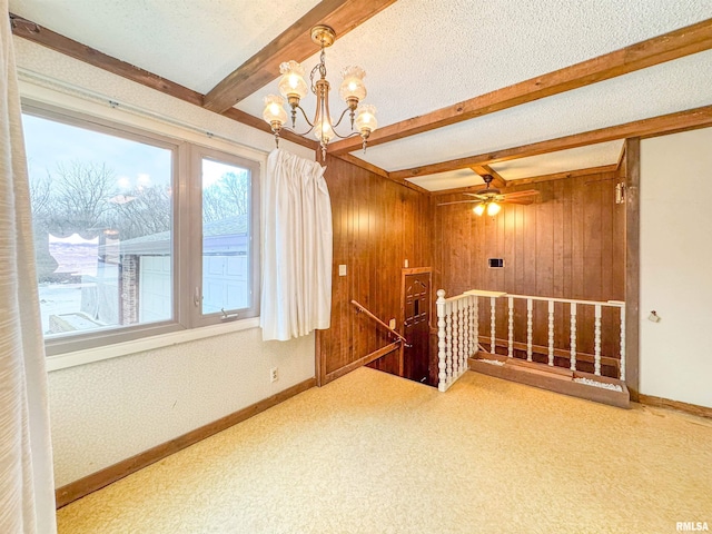 unfurnished room with ceiling fan with notable chandelier, a textured ceiling, wooden walls, and beamed ceiling