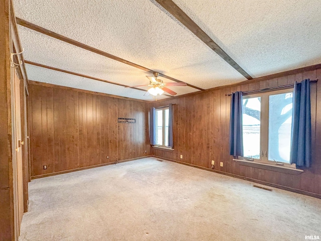 empty room with a healthy amount of sunlight, ceiling fan, beamed ceiling, and light carpet